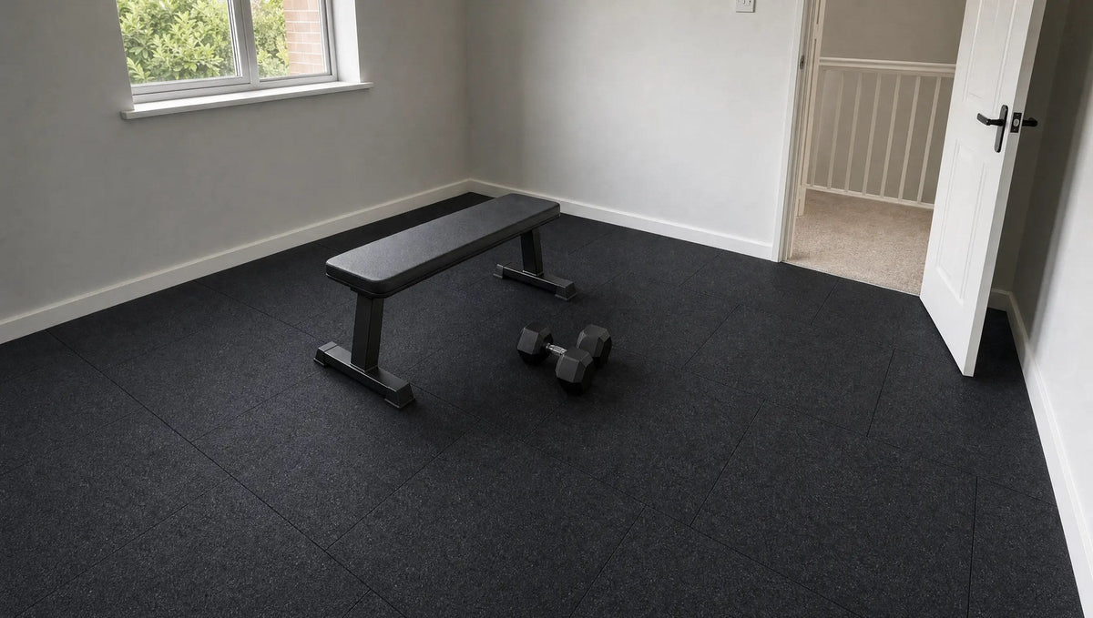 Spare room home gym floored with black 1 m rubber tiles, with a flat bench and a pair of hex dumbbells