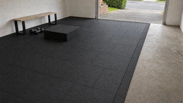 Garage gym floored with black 1 m rubber tiles in a brick pattern, an edge ramp along the open side