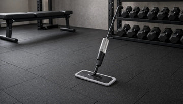 Flat microfibre spray mop on a clean black rubber gym floor laid in a brick pattern
