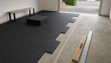 Black 1m rubber gym tiles being laid in a brick pattern on a garage floor, edge gaps still to cut