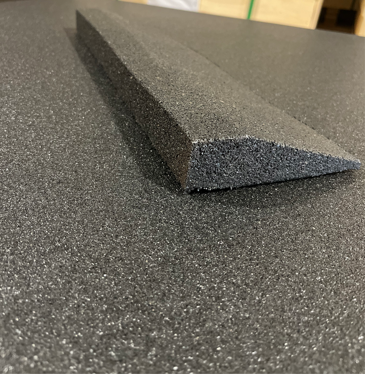 Black rubber gym flooring edge ramp resting on a rubber tile